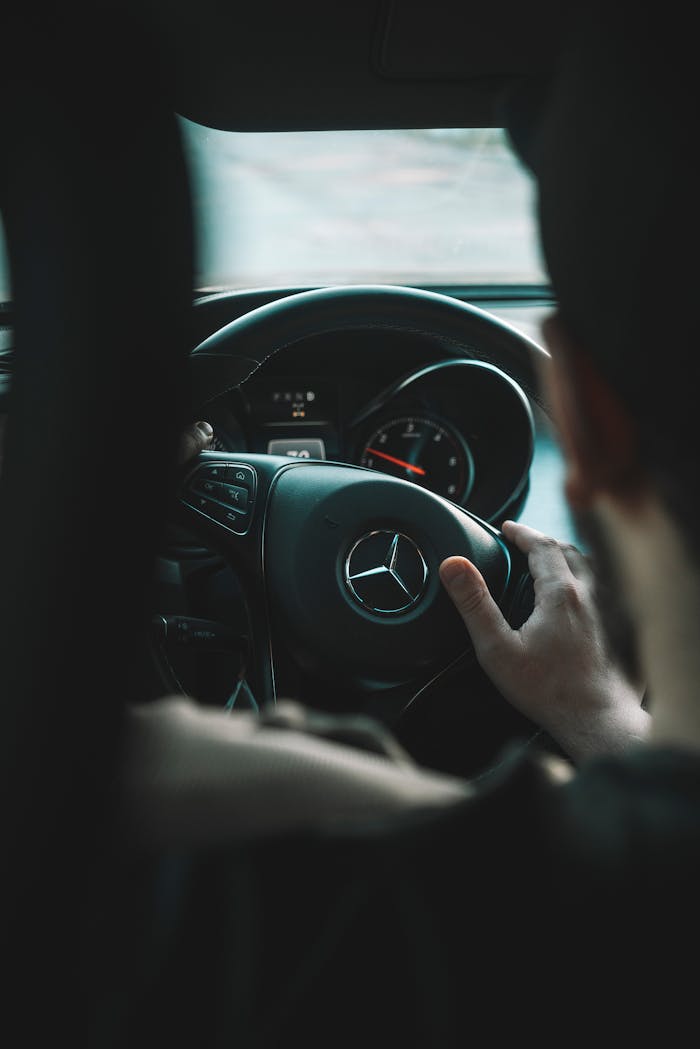 View from the backseat of a man driving a Mercedes Benz, focused on the steering wheel.